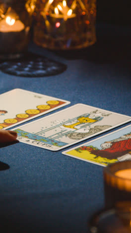 Vertical-Video-Close-Up-Of-Woman-Giving-Tarot-Card-Reading-On-Candlelit-Table-Pointing-Out-Ace-Of-Cups-Card